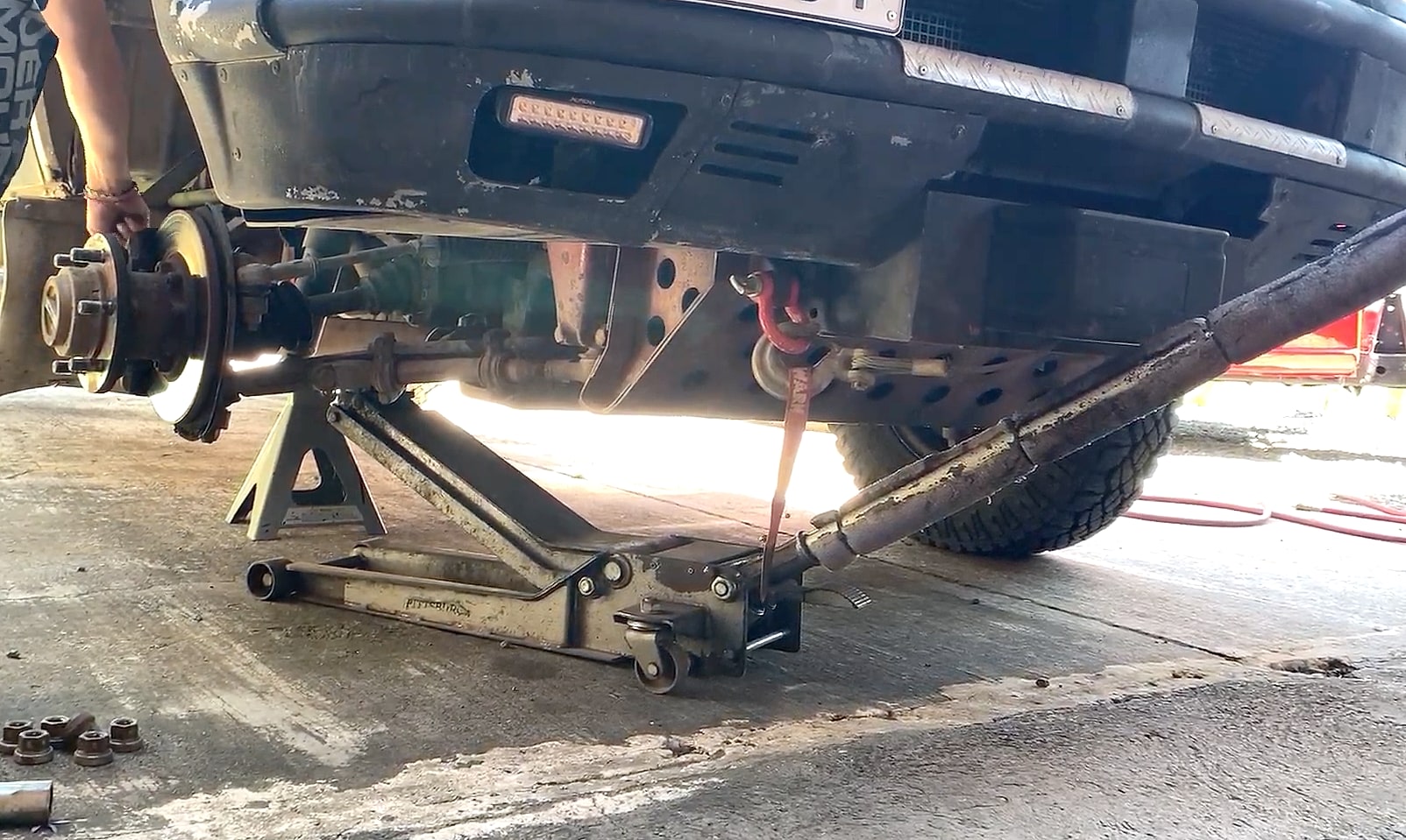A vehicle raised on a trolley jack and axle stand with a wheel removed