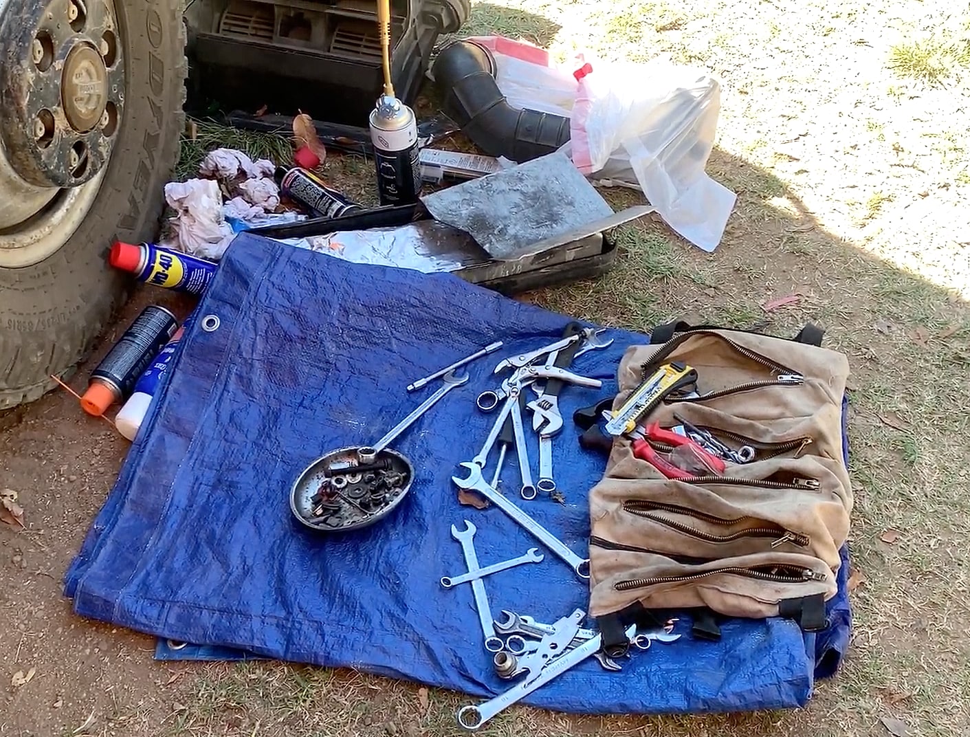 Spanners and a canvas tool roll laid out on a tarp beside a wheel